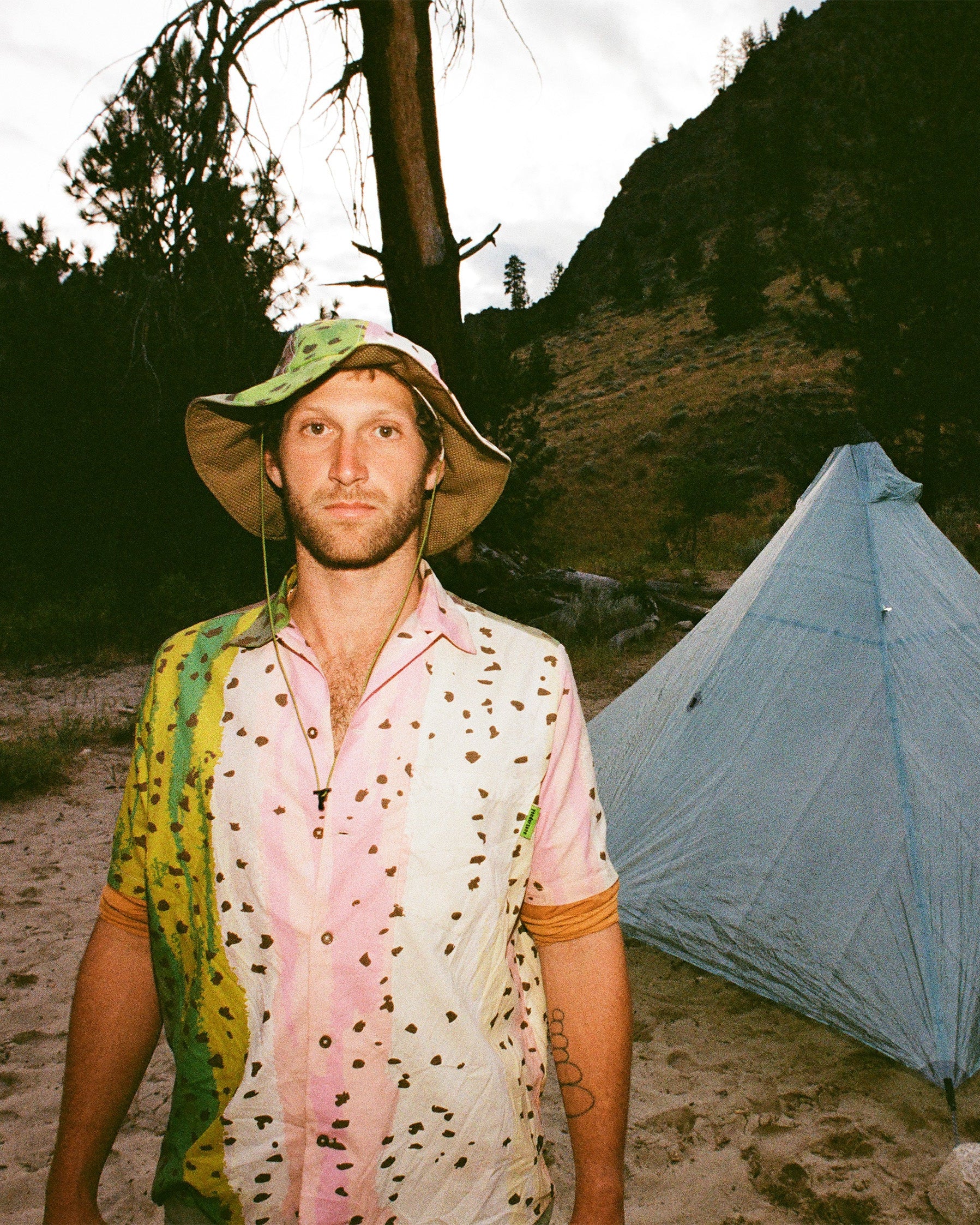 Man standing in a mountainous area with a tent in the background